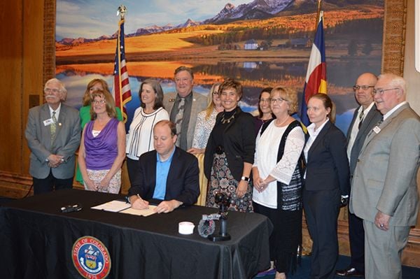 Attorney Shari Caton looks on as Governor Jarod Polis signs the “Office of Public Guardianship” legislation.